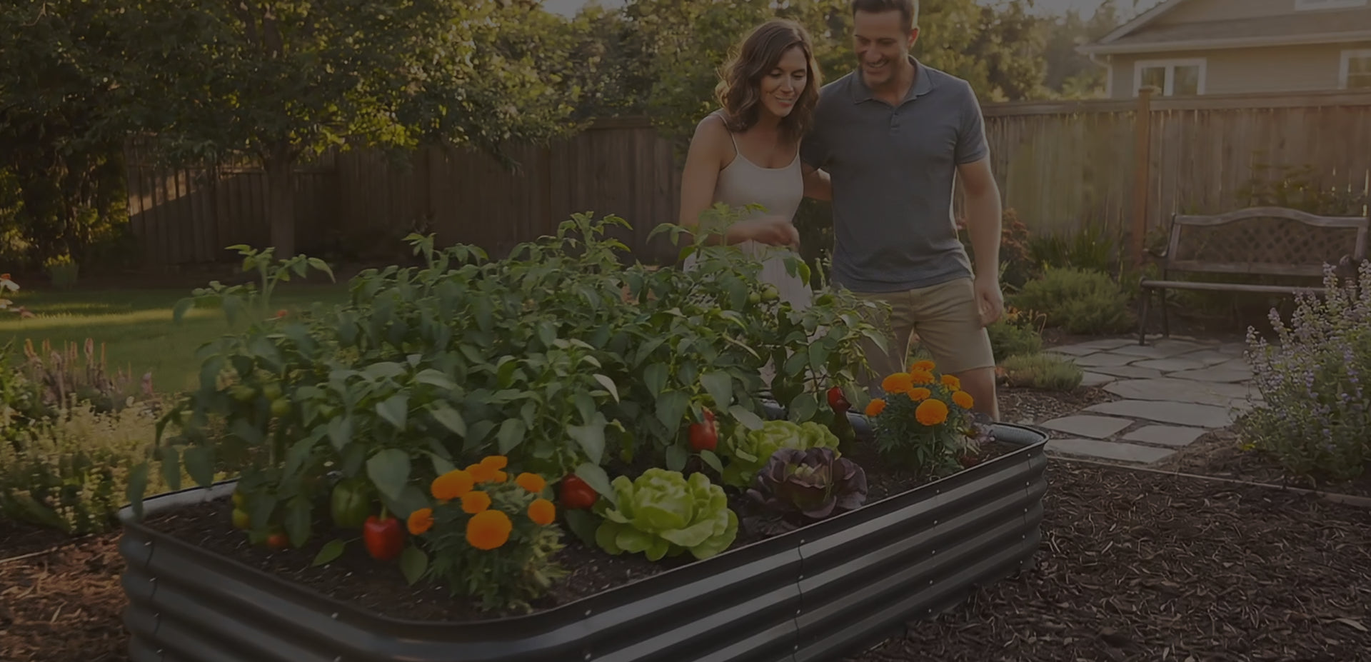Man and woman standing next to a raised garden bed filled with plants and flowers in a backyard setting.